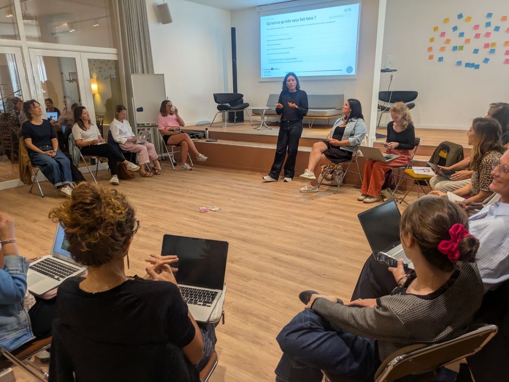 Laetitia Armange anime un atelier : les participants, assis en cercle avec leur ordinateur portable, l'écoutent devant l'écran de présentation.